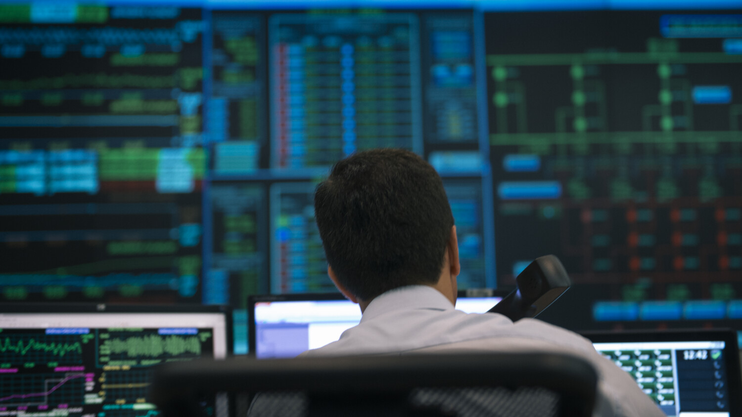 A person working for an energy utilities company in front of computer screens showing large amounts of data