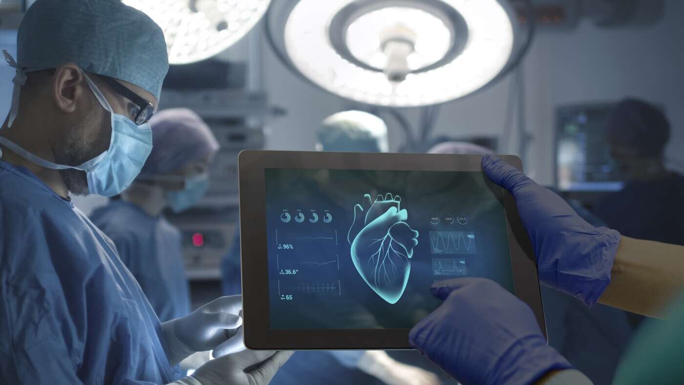 Cirujanos en operación cardíaca usando tableta con imagen del corazón y datos médicos.