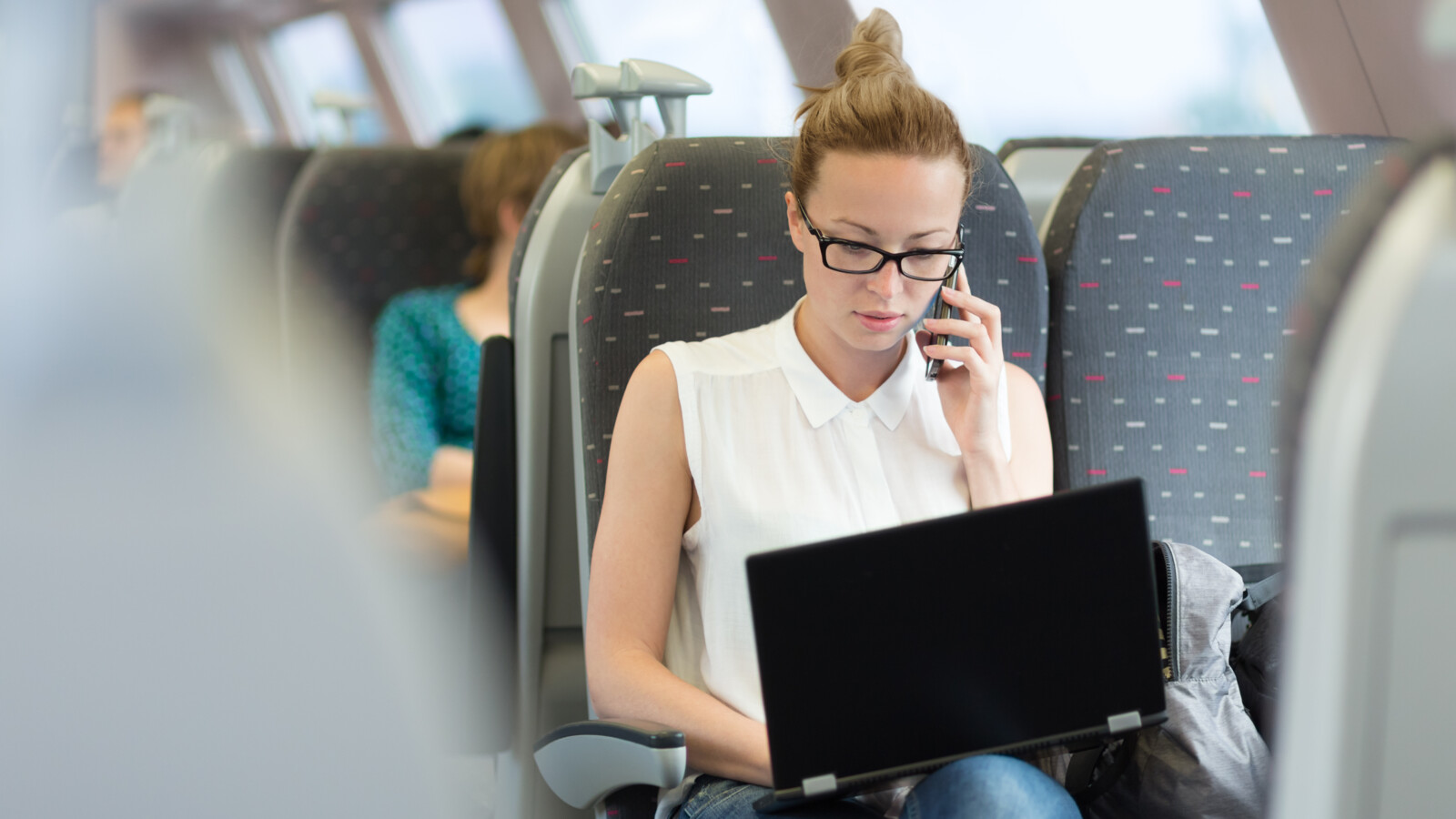 Person on train using laptop and talking on mobile phone.