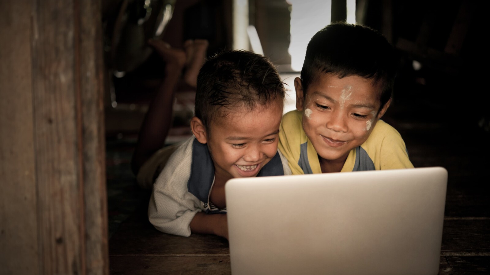 兩個孩子躺在地板上看筆記型電腦螢幕。