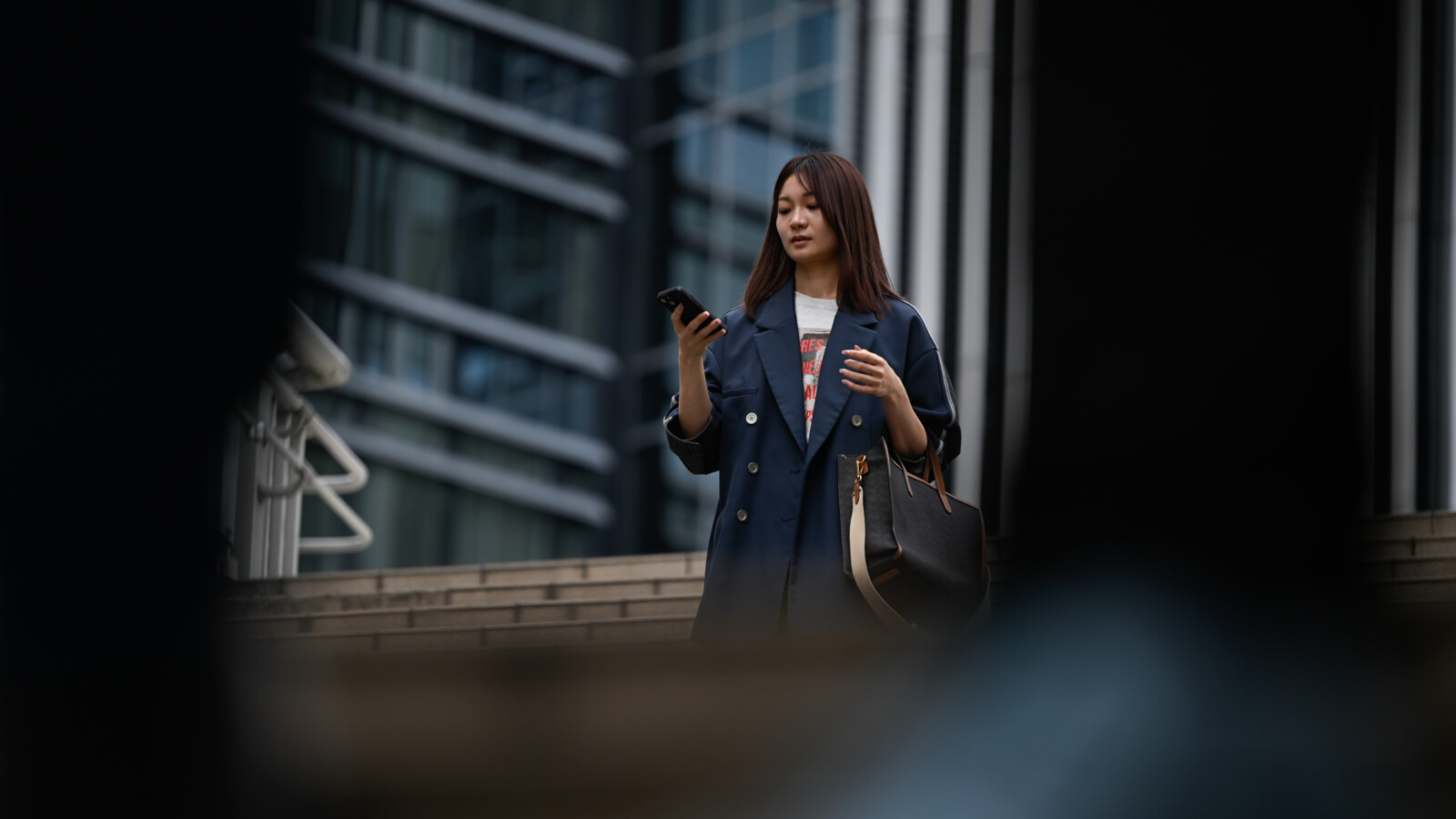 A woman staring on her mobile with an office building in background.