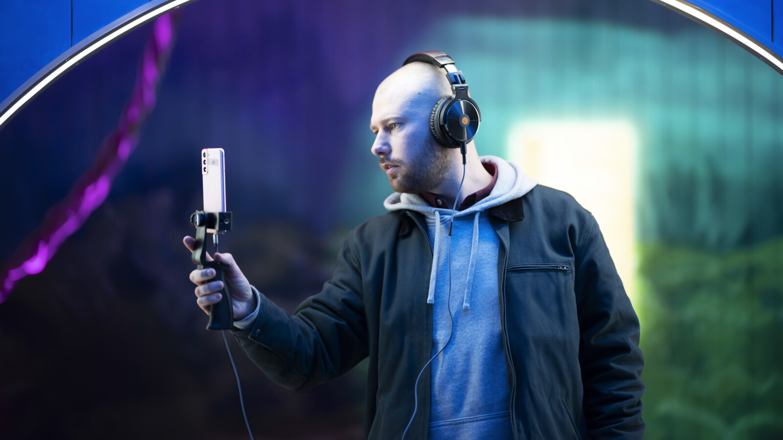 Man holding phone using AR, wearing headphones and with a blue archway behind him.