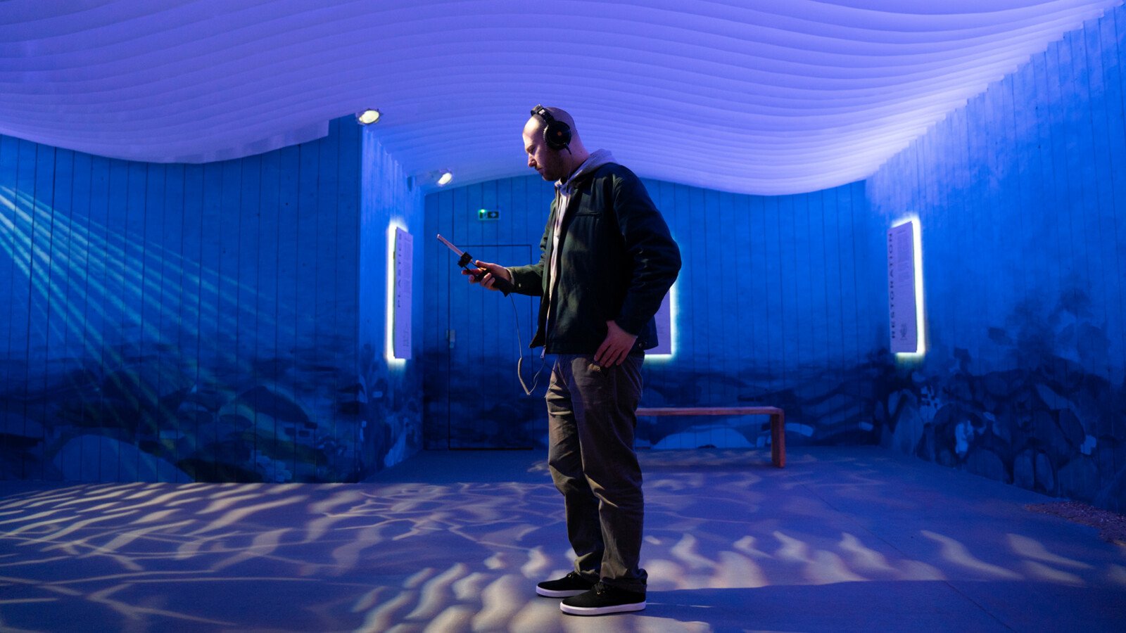 A young man is at an interactive exhibition experience  using his mobile phone and wearing headphones