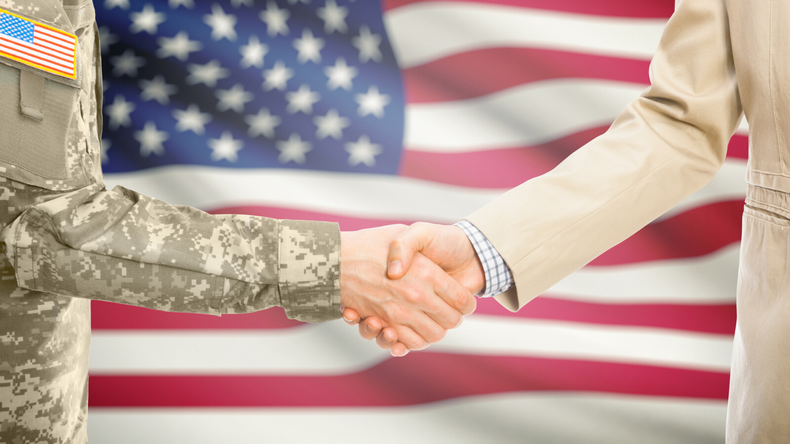 Persons shaking hands in front of the US flag.