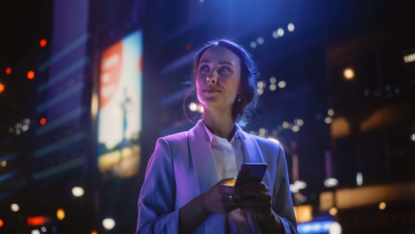 A smiling young lady holding a smartphone amid city lights