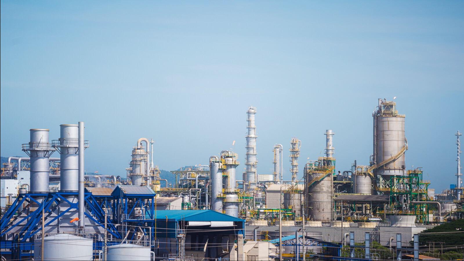 Industrial complex with chimneys, tanks, and blue sky.