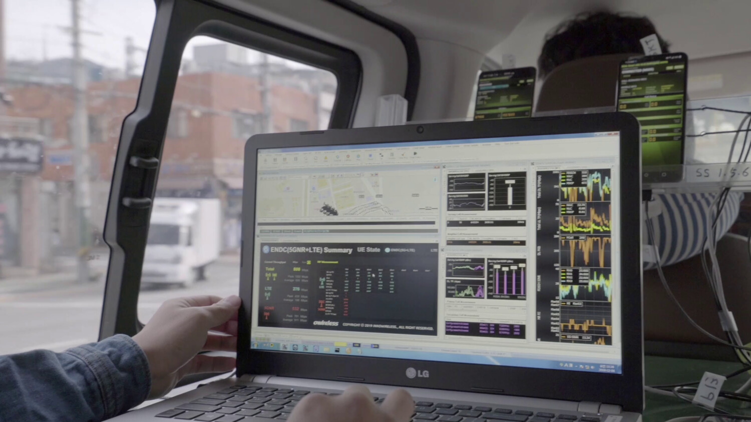 Person in vehicle using laptop with data on multiple screens.