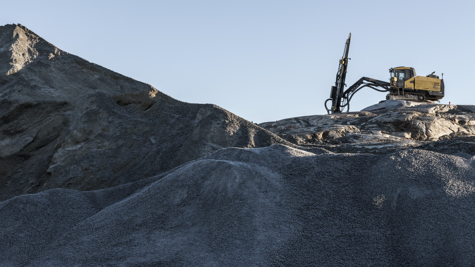 Excavator with drill on rocky terrain.