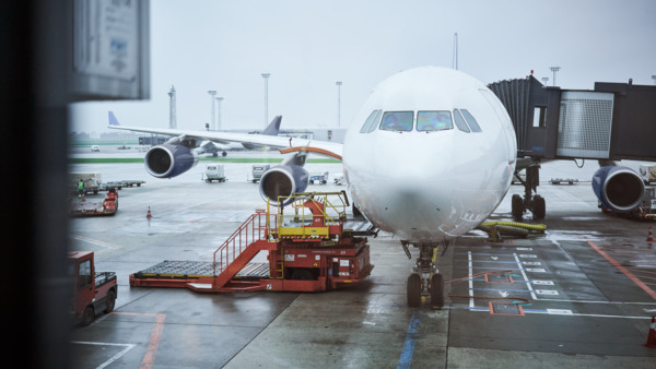 Airplane at gate with jet bridge and ground support vehicles.