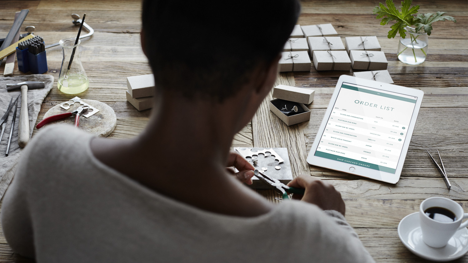 Woman making jewelry next to a tablet and tools.
