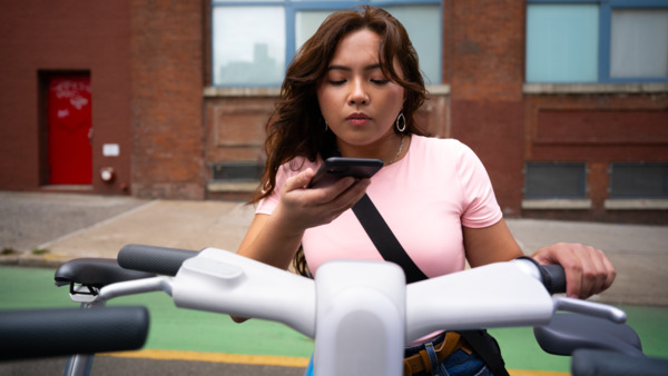 A person on an electric scooter uses a smartphone on a city street.