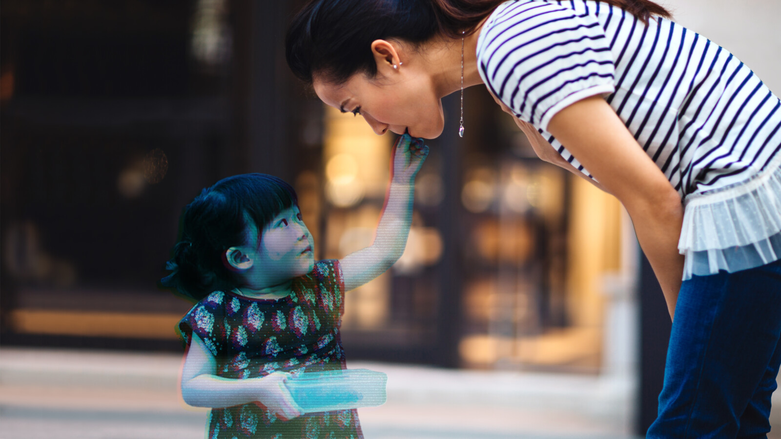 A hologram image of a young girl touching the cheek of a woman bending in front of her.