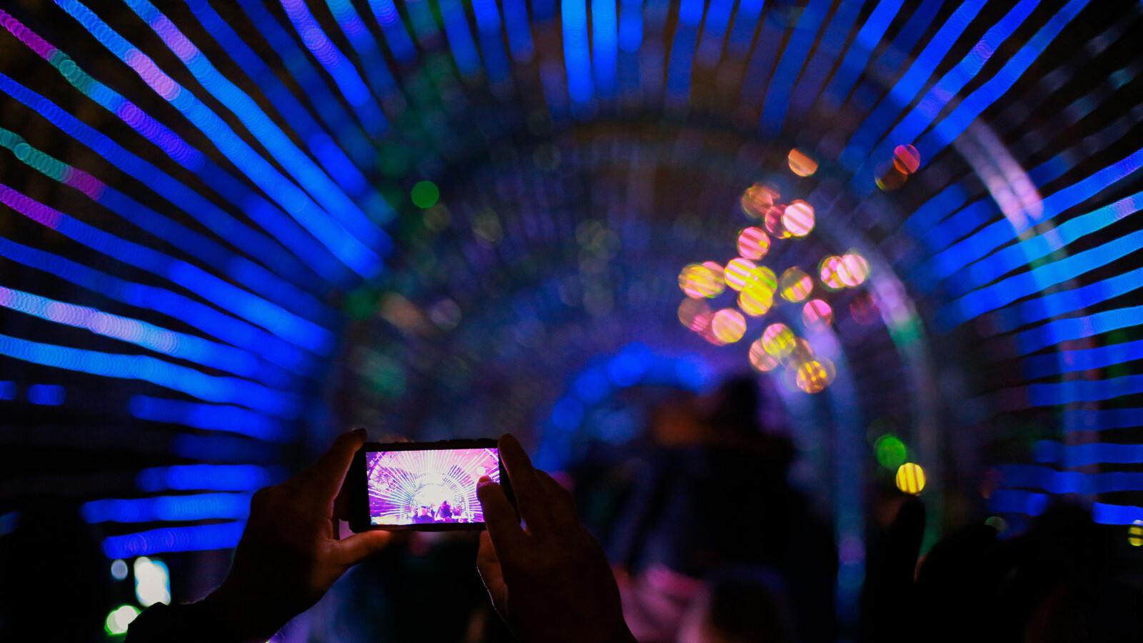 Person films colorful light tunnel with smartphone.