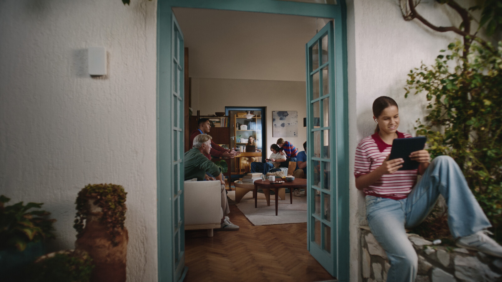 People relaxing and using a tablet in a cozy home, seen through open doors.