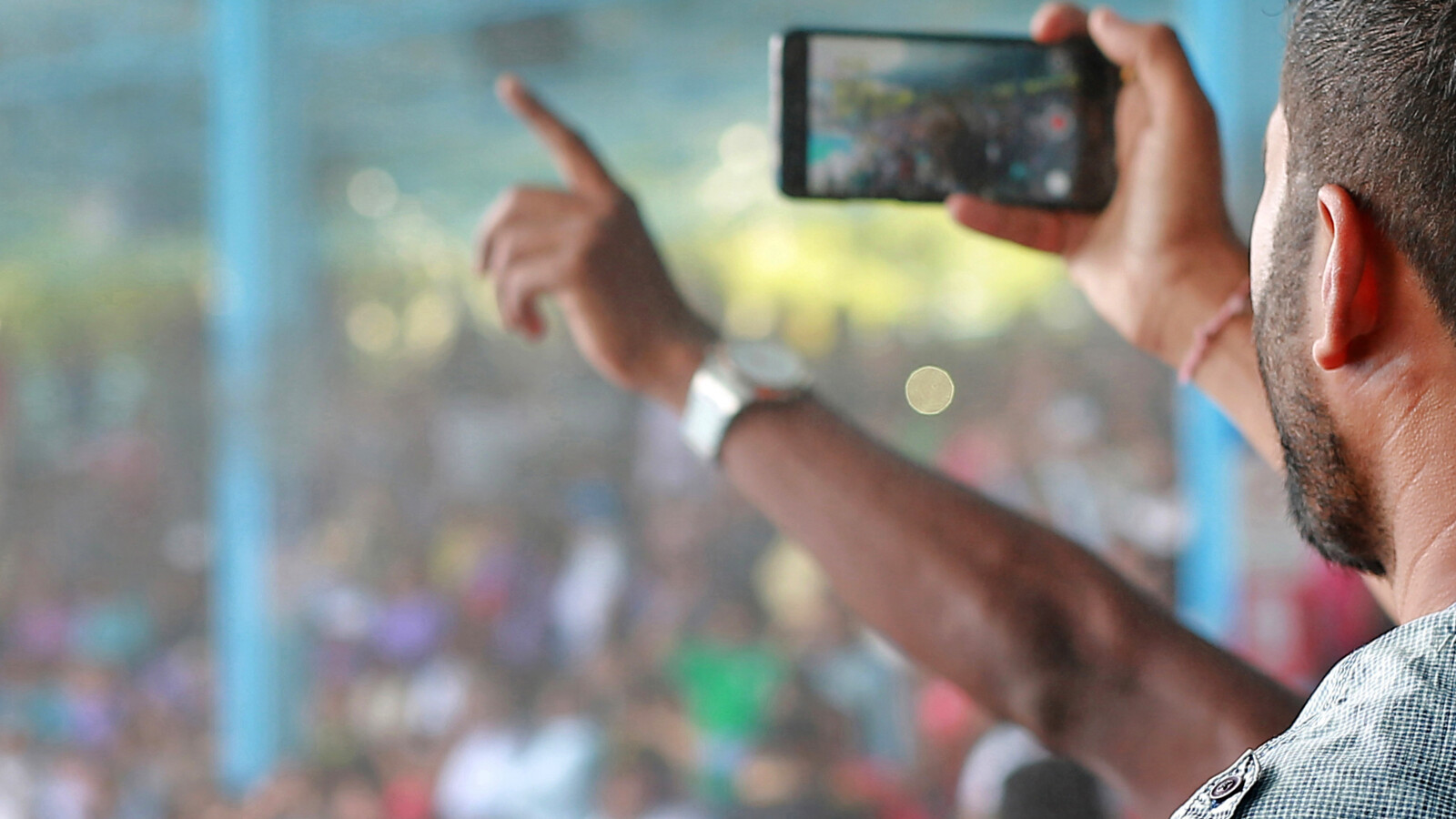 Person at a stadium event, filming with mobile phone.