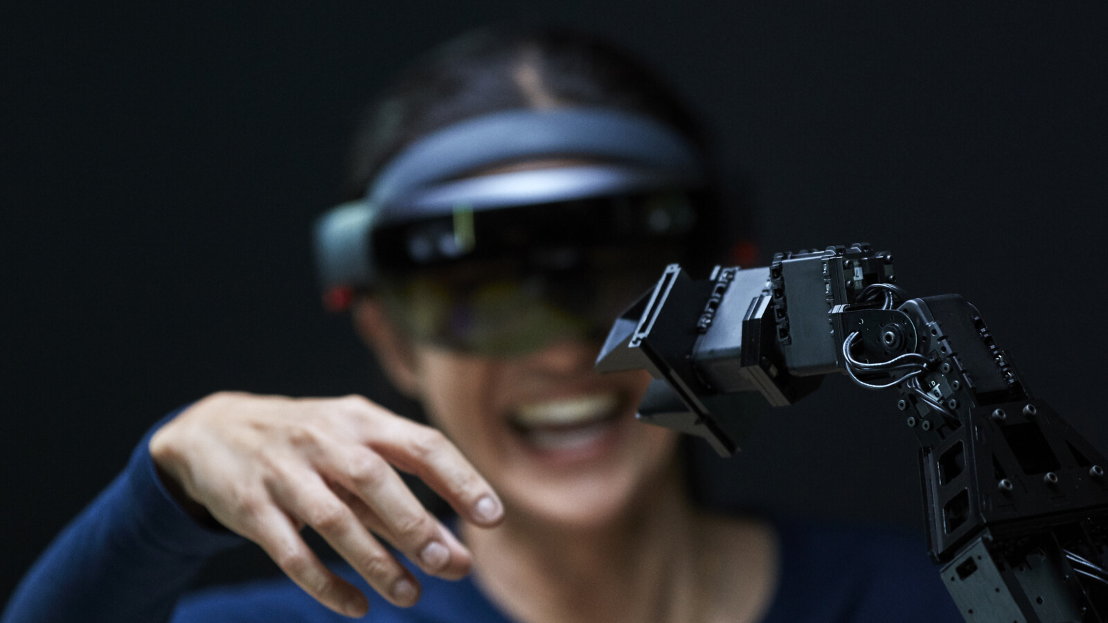 Woman using AR glasses interacting with robotic arm.