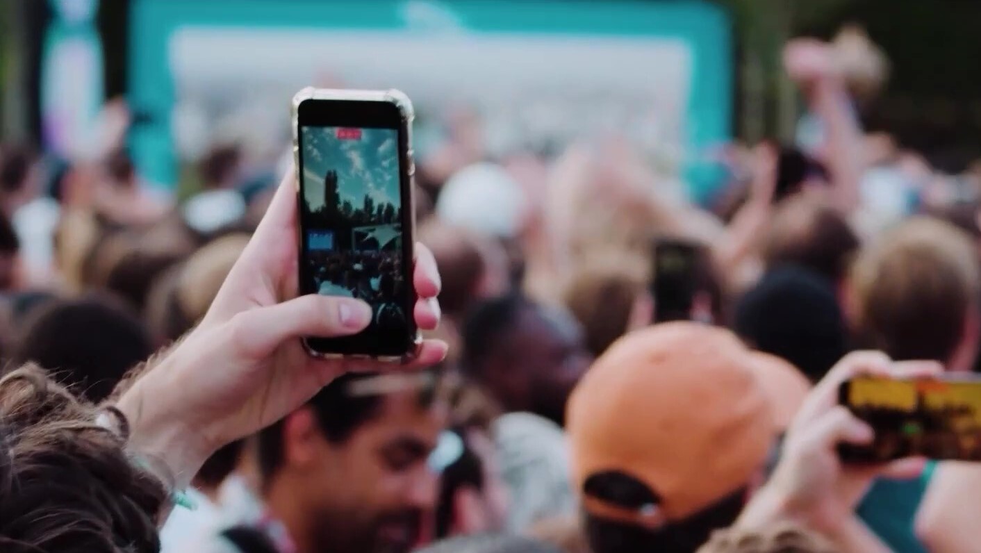 Person holding mobile telephone, filming an event.