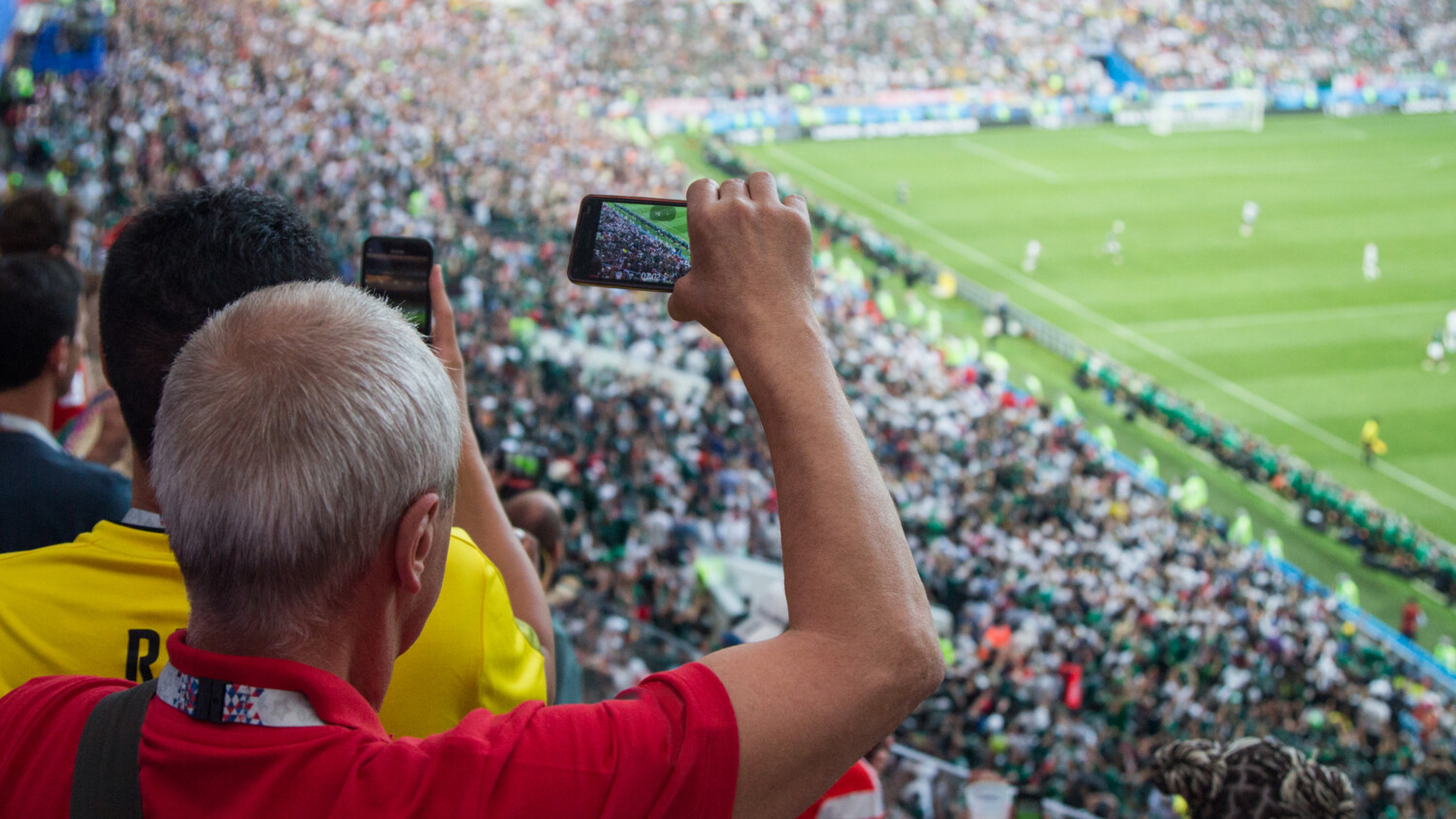 Football supporters filming the match with their mobile phones.
