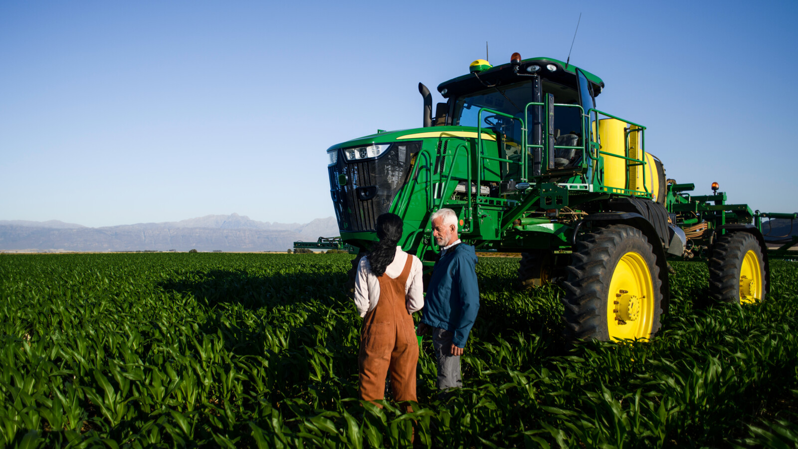 A man and a woman with a connected tractor in a field of crops.