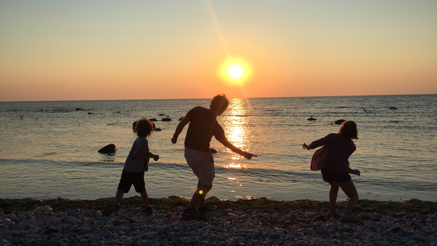 Parent playing with kids in the sunset on a beach.
