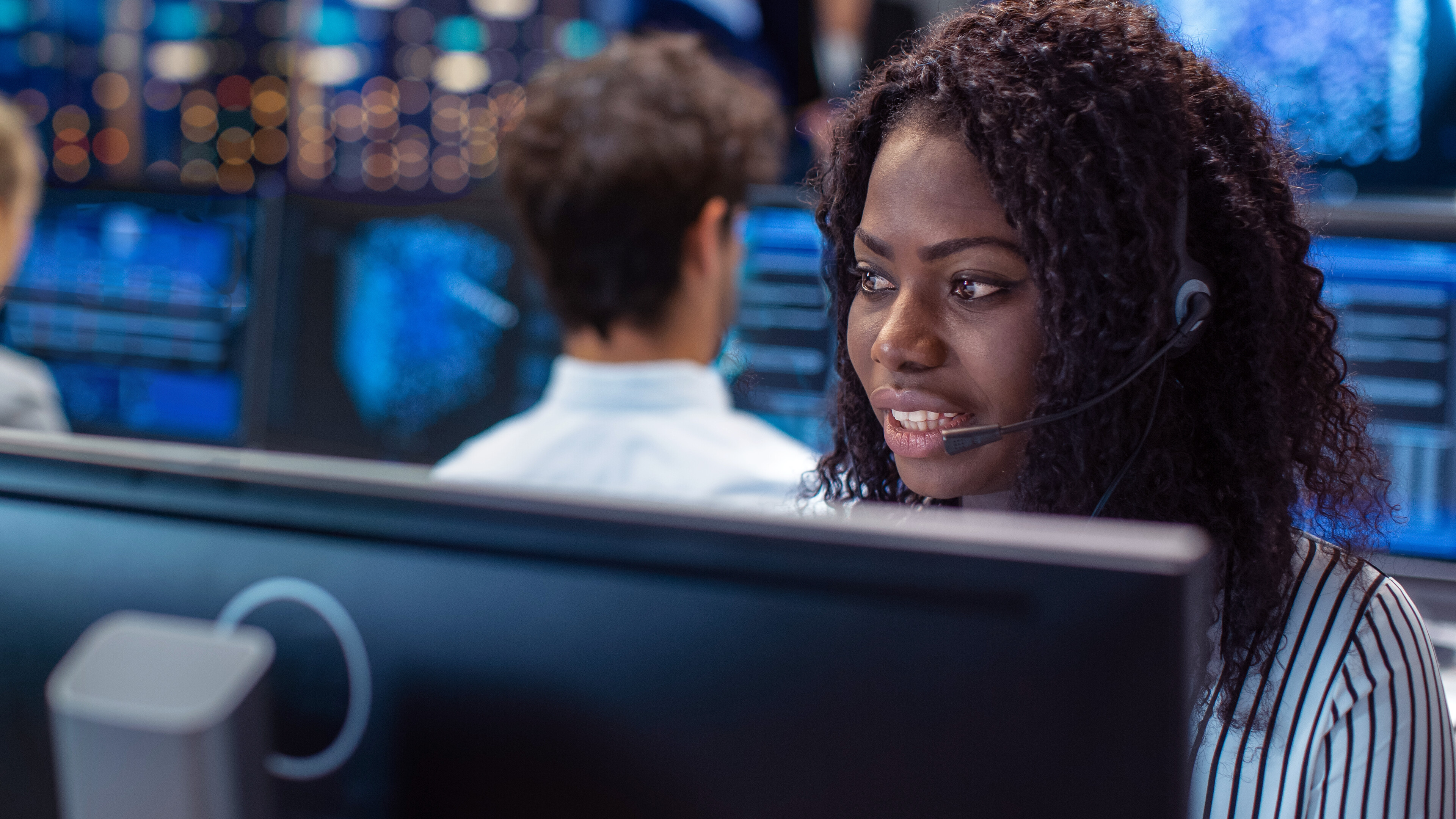 Person with headset in front of computer screens.