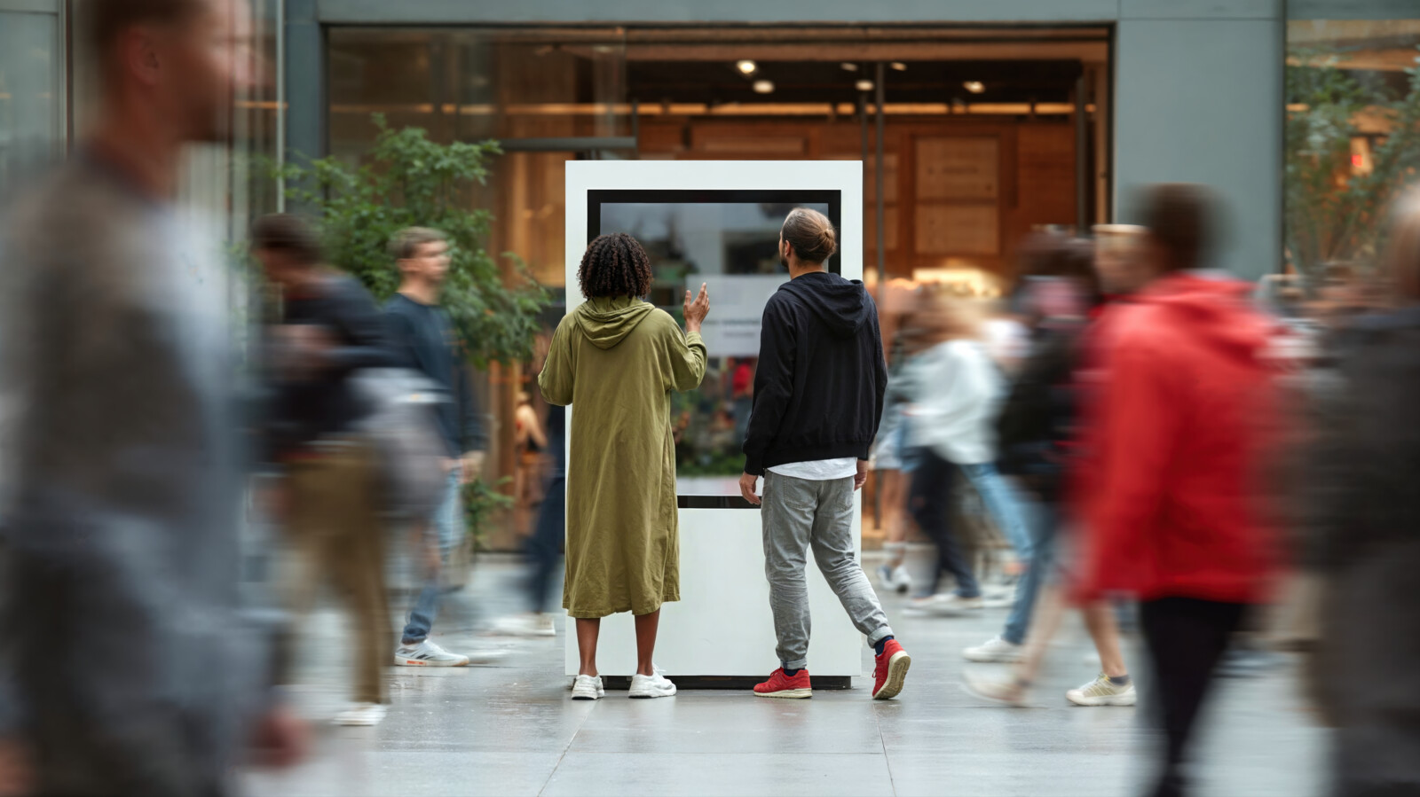 Two people interacting with digital display kiosk in busy public space with motion blur crowd