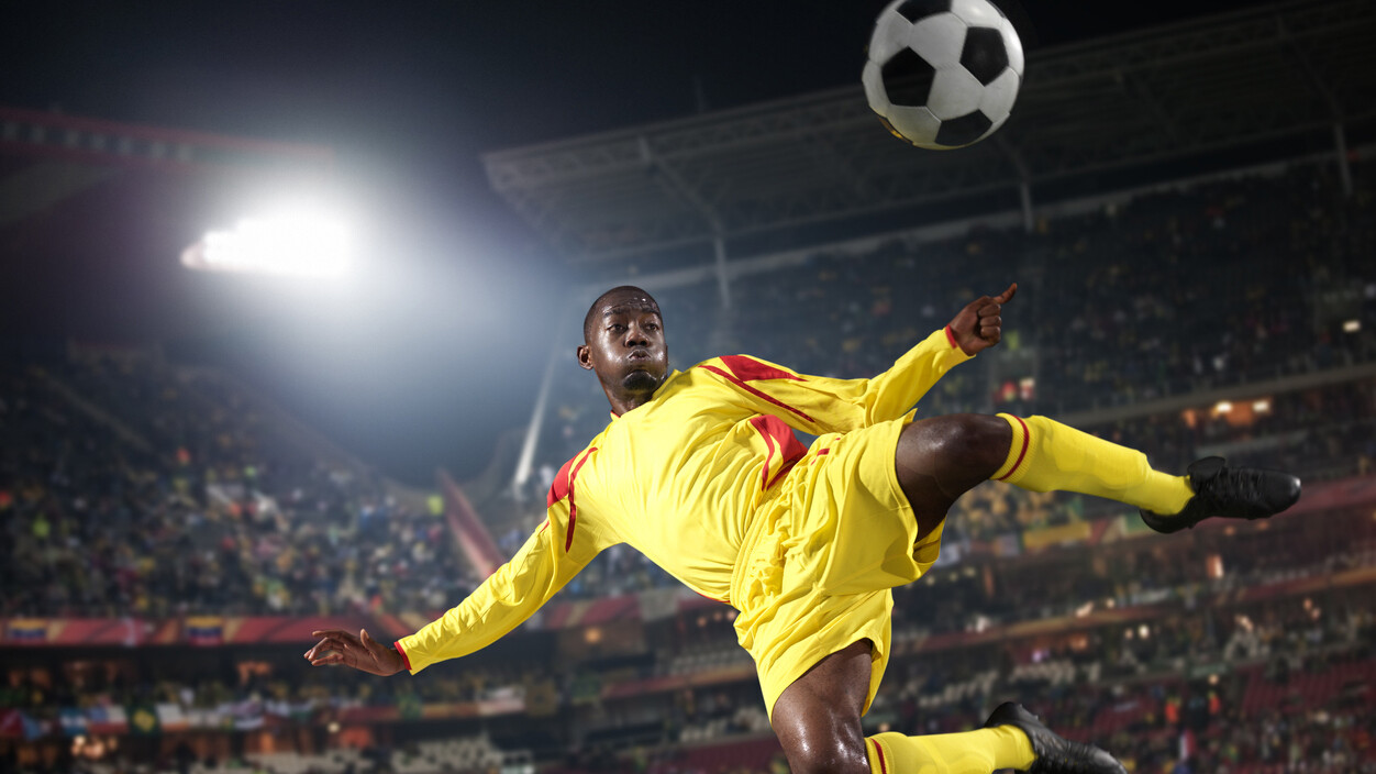 Soccer player in yellow kicks ball mid-air in stadium.
