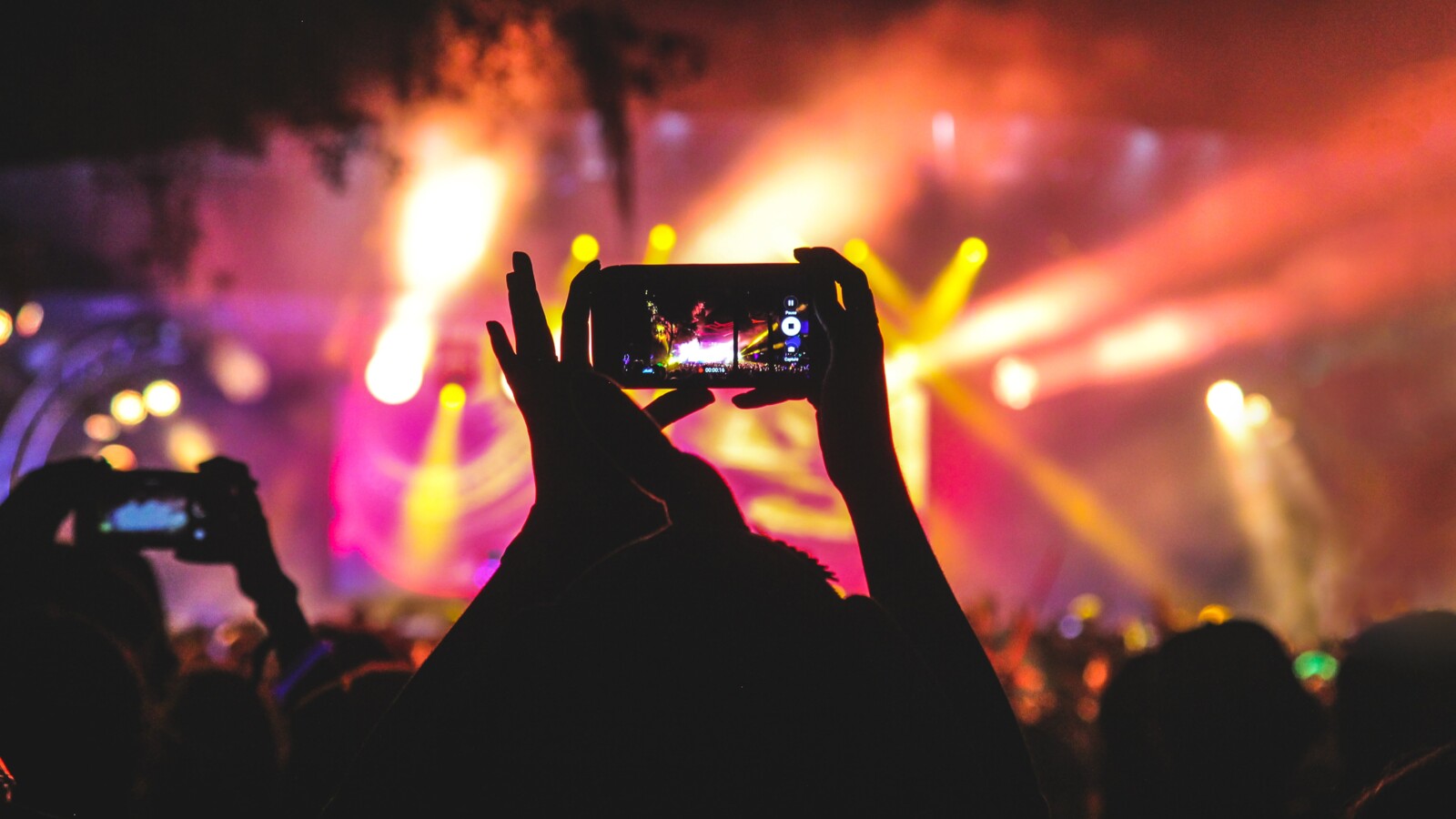 Hands holding smart phone, filming at a concert event.
