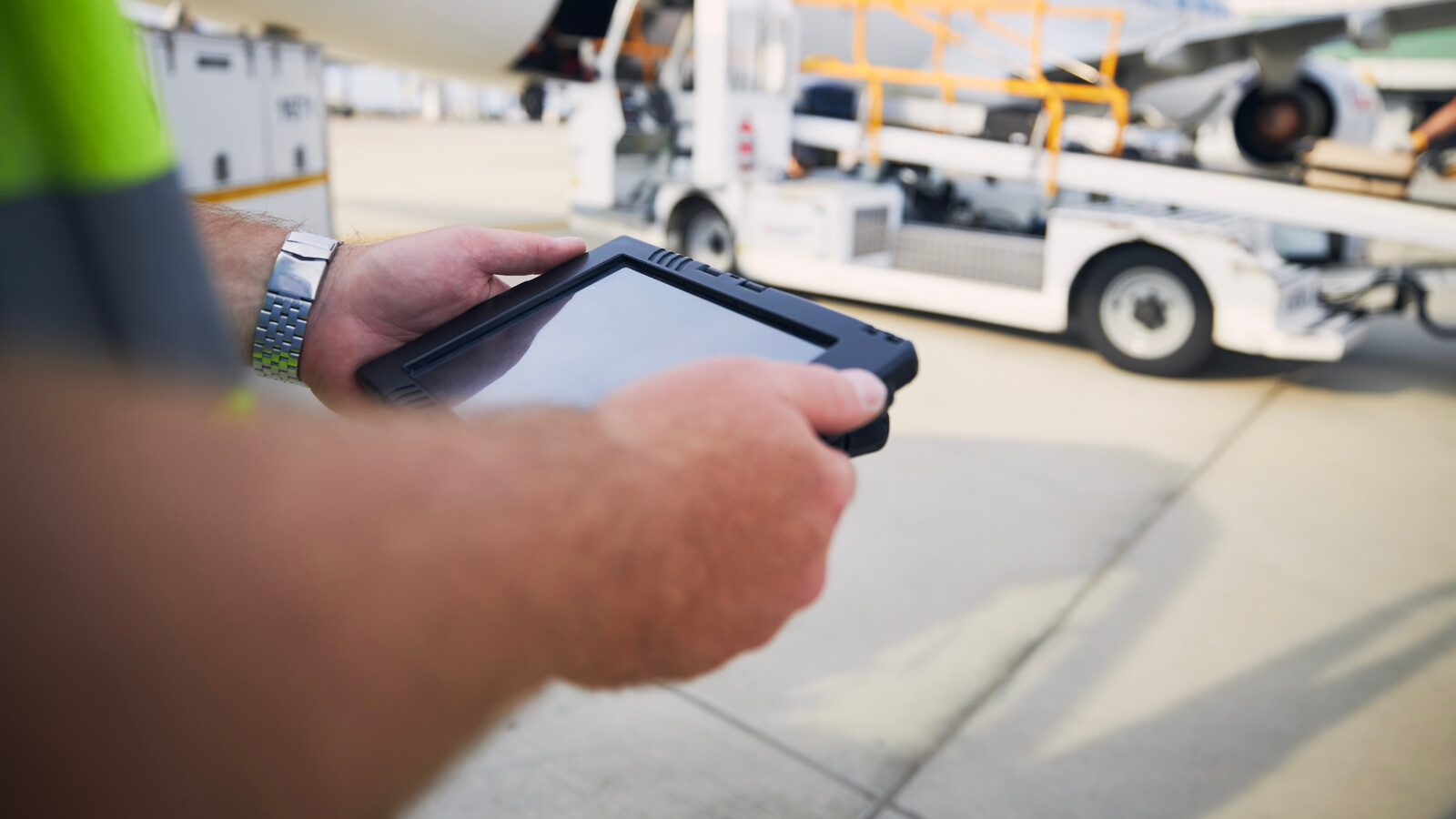 Person holding tablet near airport ground service vehicle.