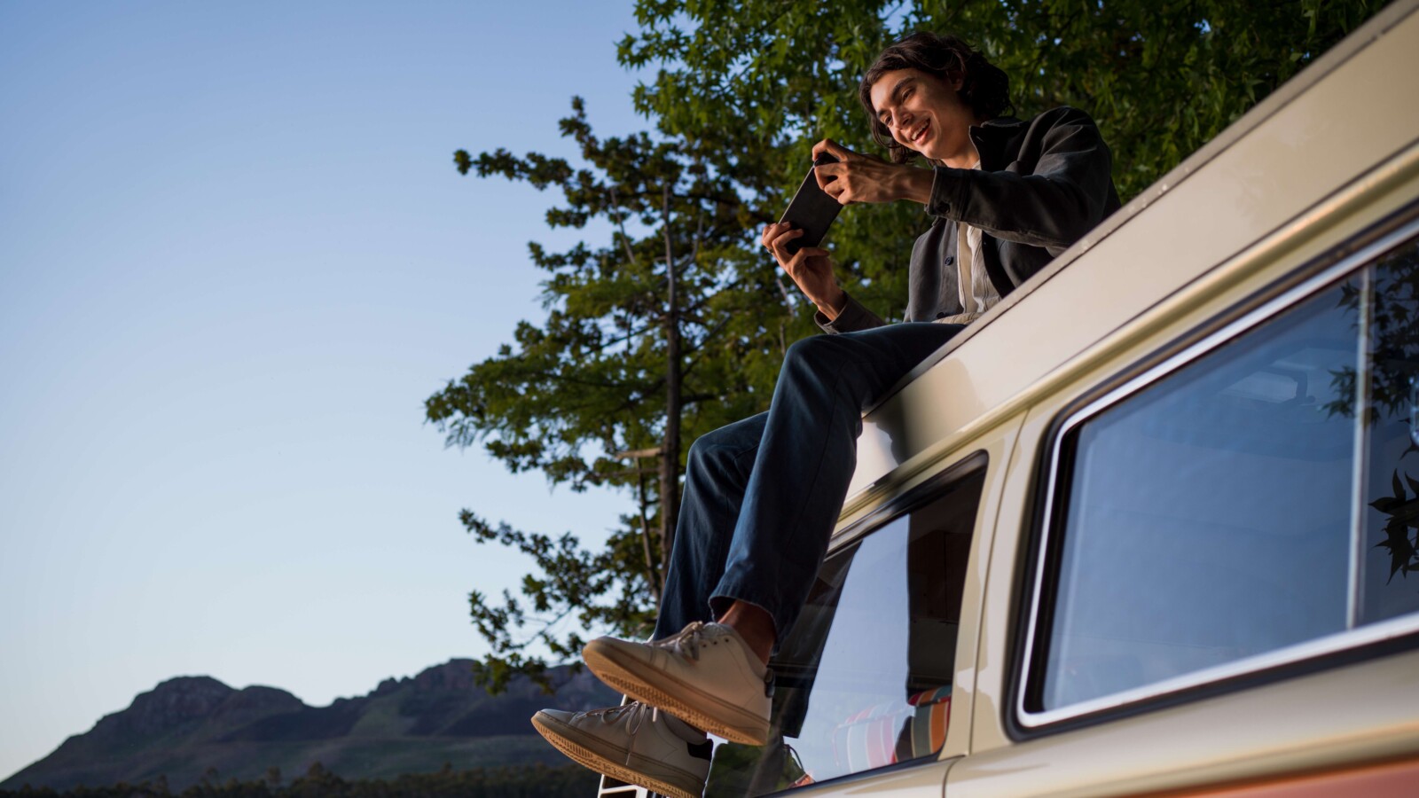 Person sitting on the roof of a van, gaming on his mobile phone.