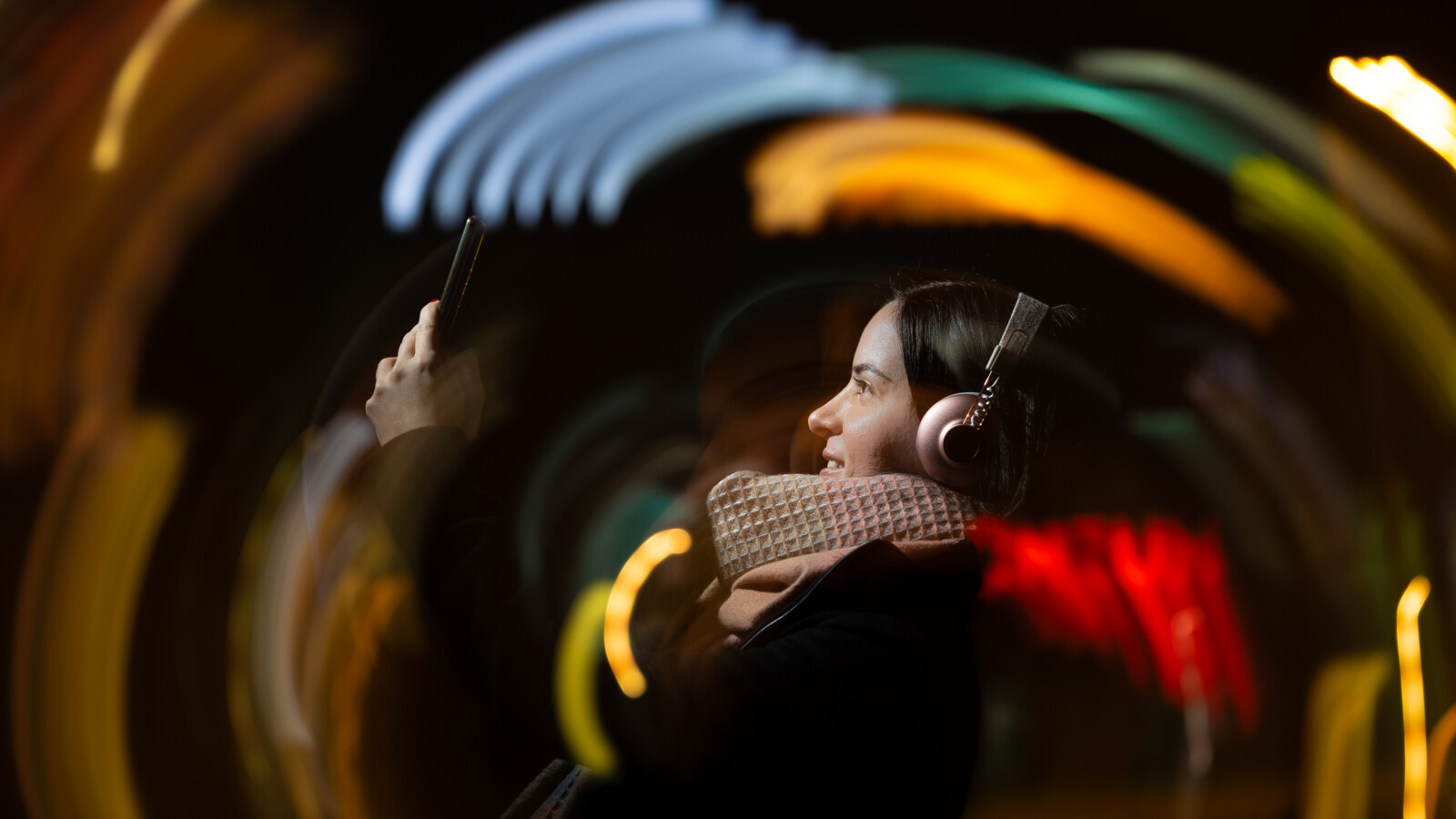 Woman with headphones holding up mobile phone.