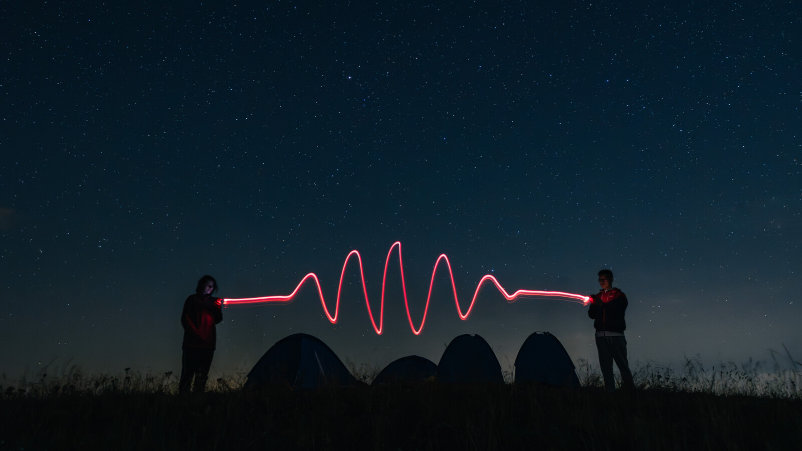 Two figures create a light trail under a starry sky