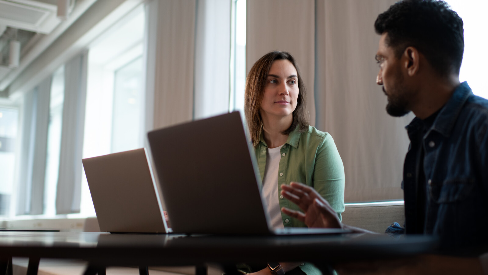 Two colleagues talking while working on their laptops