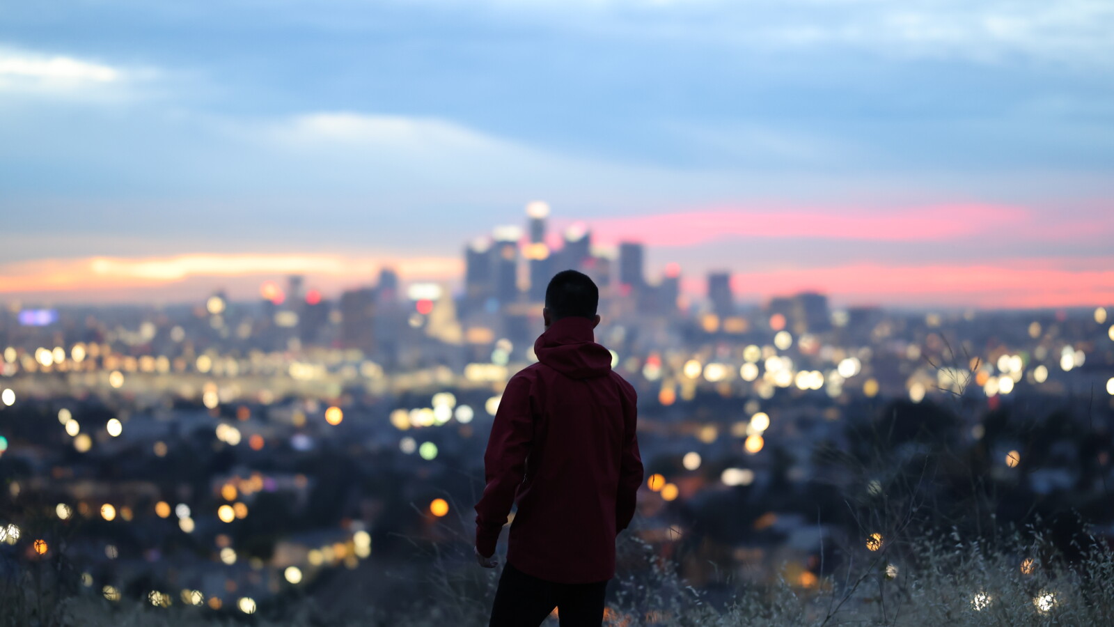 Person overlooking city lights at sunset from hill