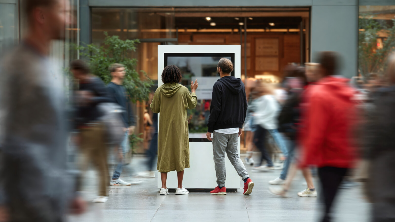 Two people interacting with digital display kiosk in busy public space with motion blur crowd
