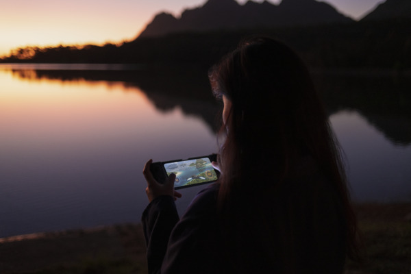 A person uses a smartphone while overlooking a body of water.