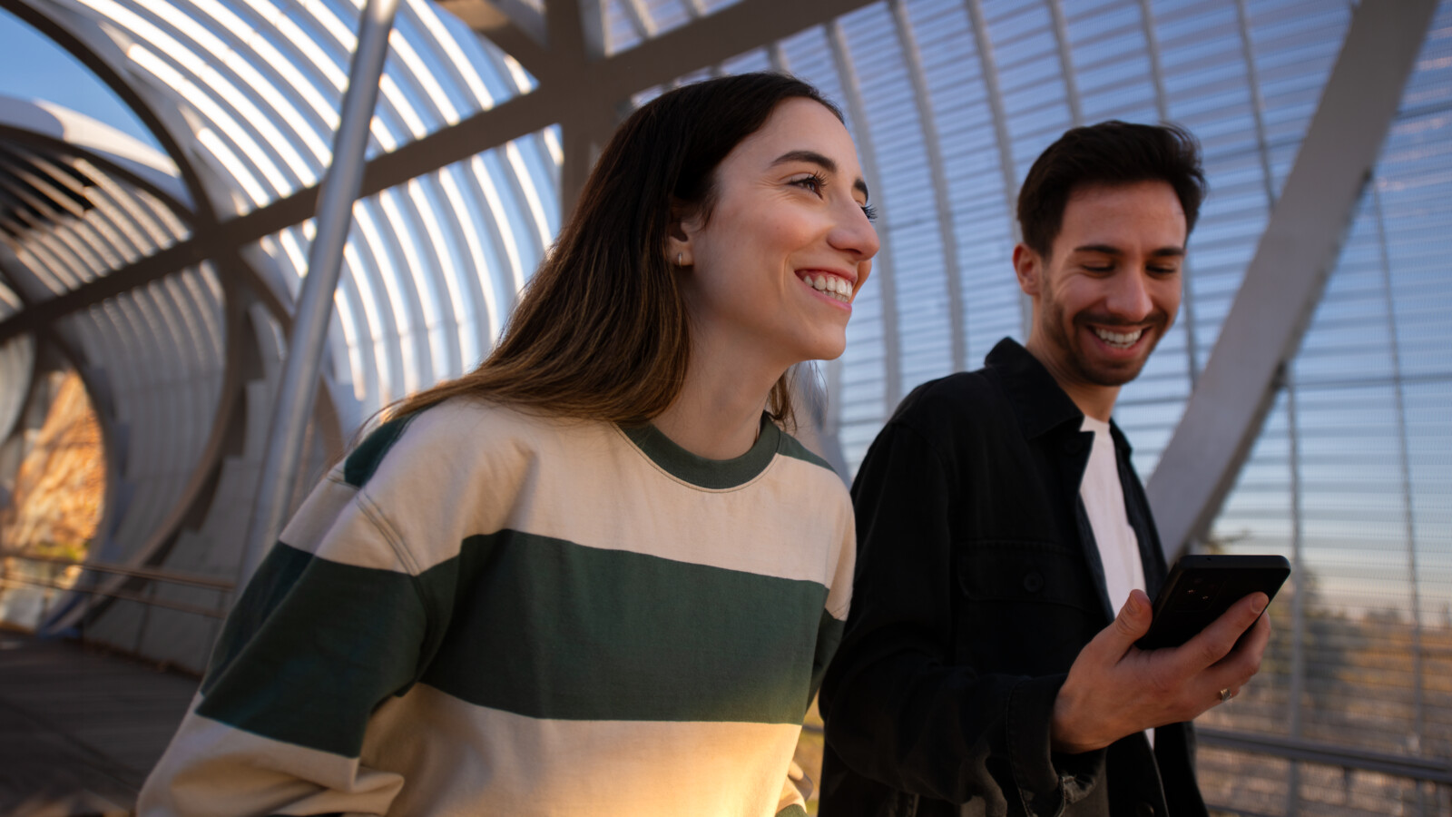 Two people smiling and walking on a bridge.