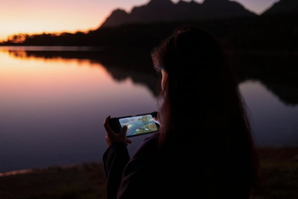 A person uses a smartphone while overlooking a body of water.