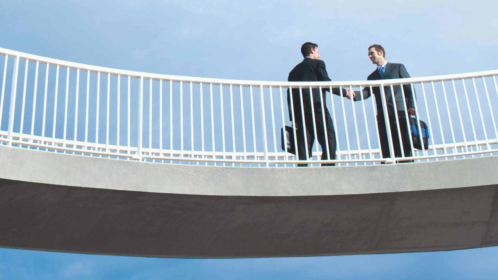 Two persons shaking hands on a bridge.