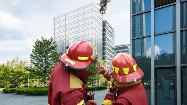 Firefighters watch smoke rise from building.