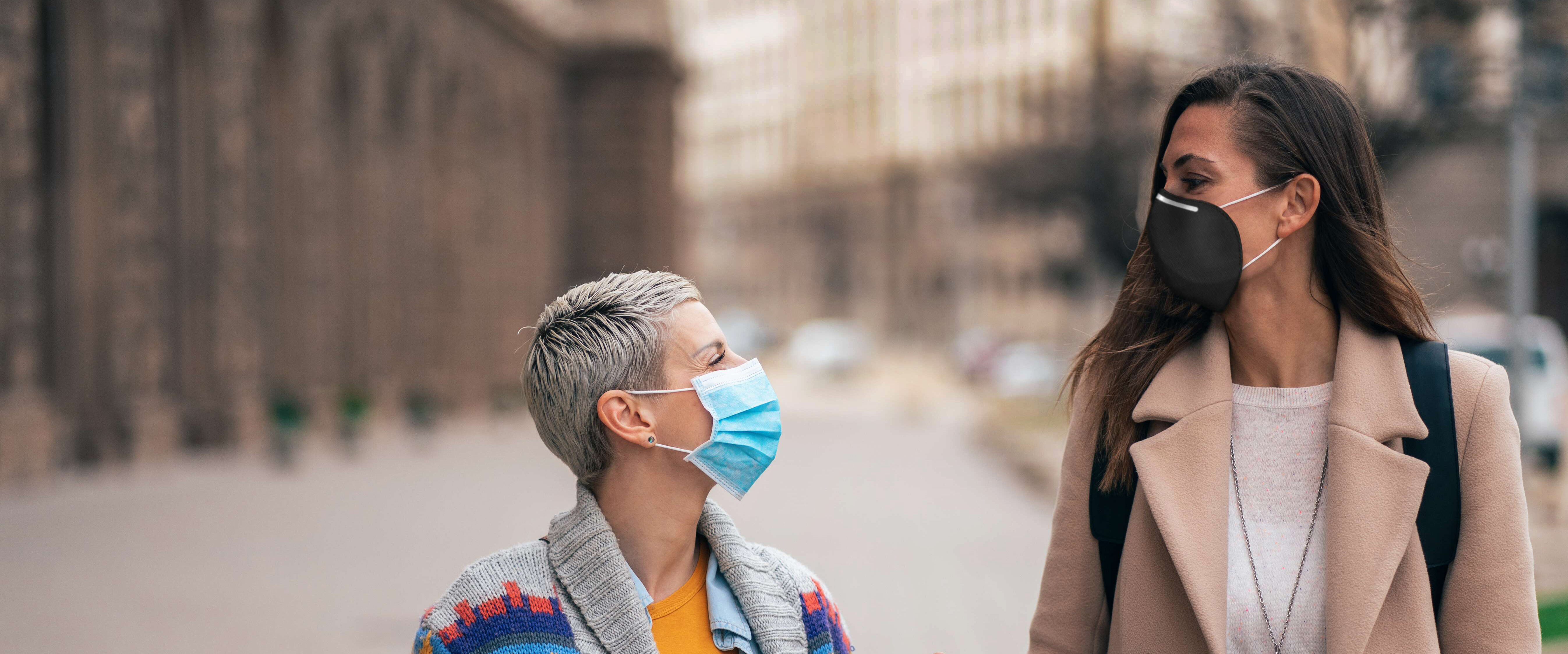 Two women during the pandemic wearing masks talking.