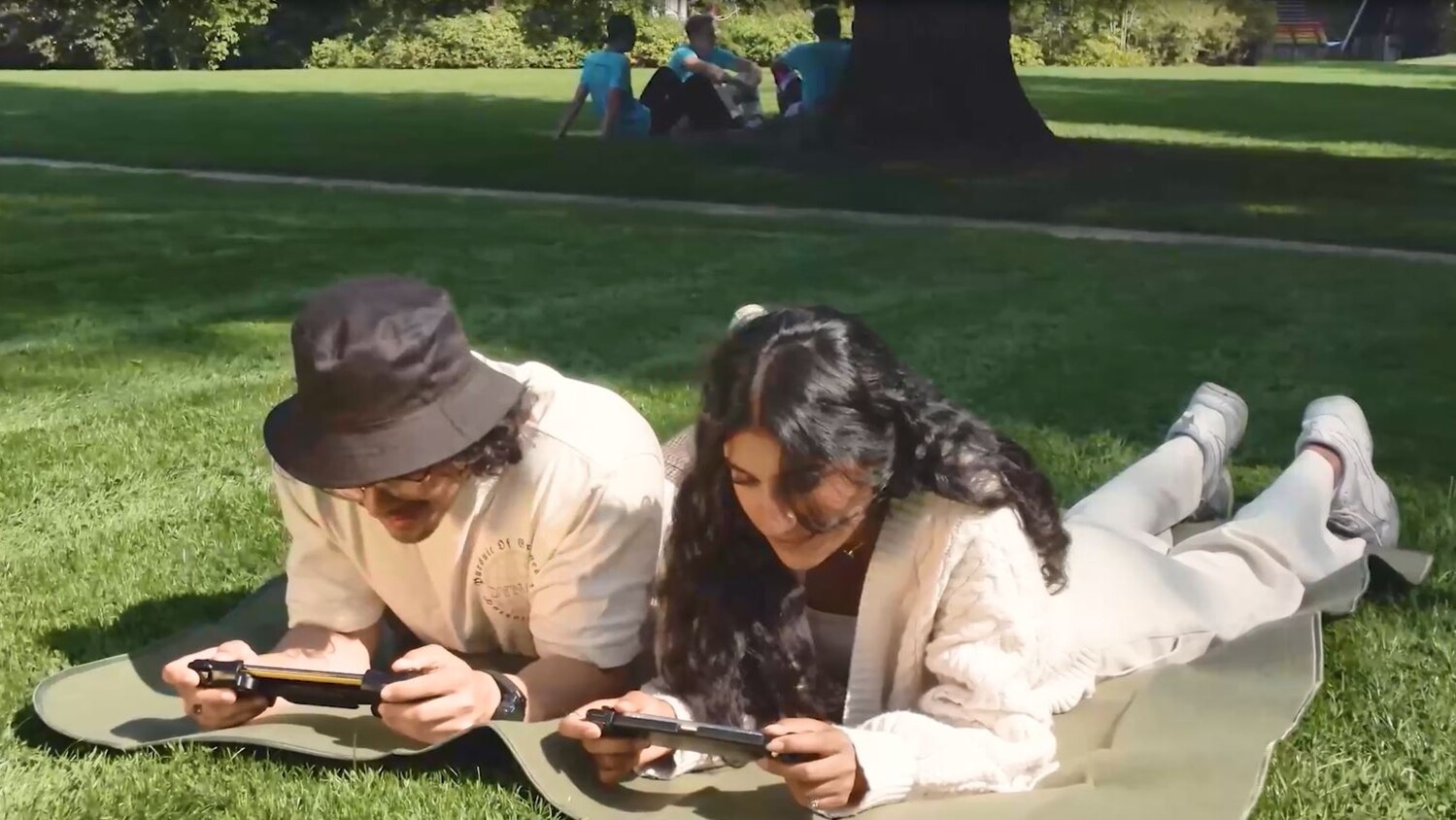 Two persons on a picnic blanket in a park with mobile devices.