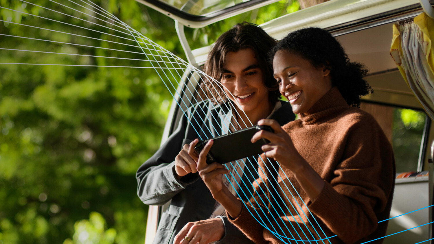 Two people near a van outdoors, looking at a device.
