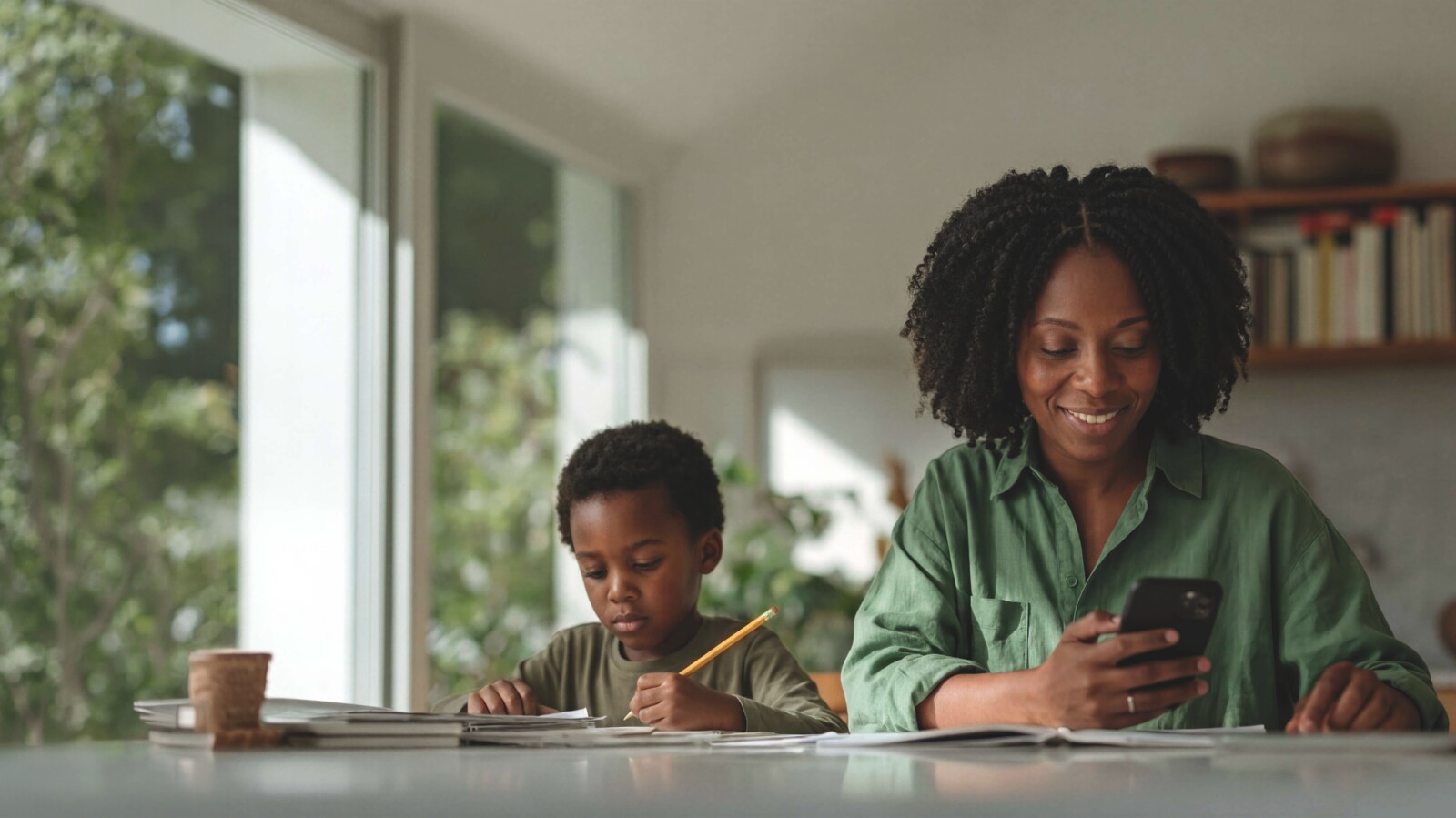 Mother paying bills with smartphone while child doing homework at table