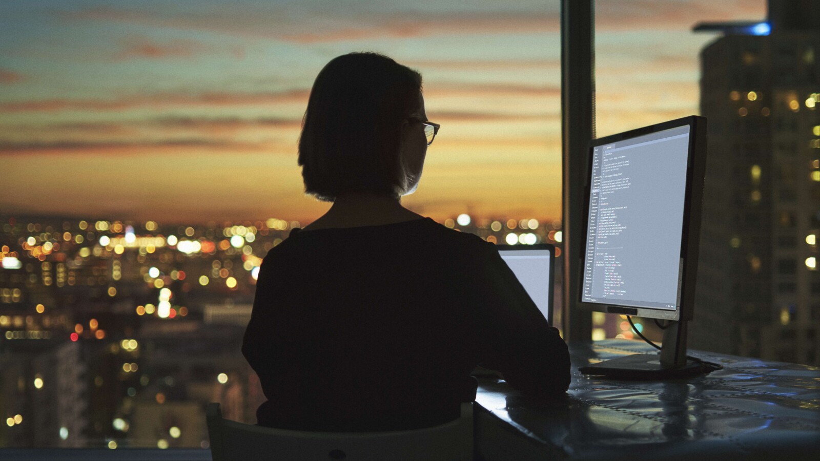 Woman working in front of computer screen at dusk.