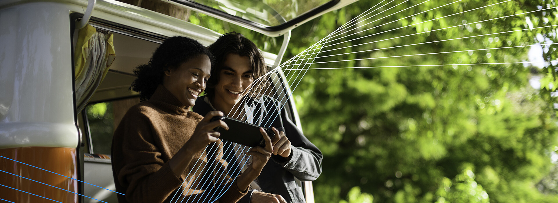 Two people near a van outdoors, looking at a device.