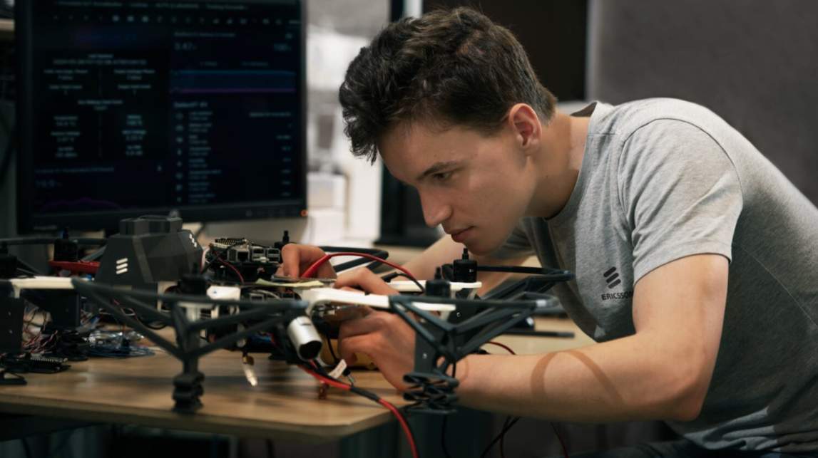 Person repairs drone at desk with tools and monitors.