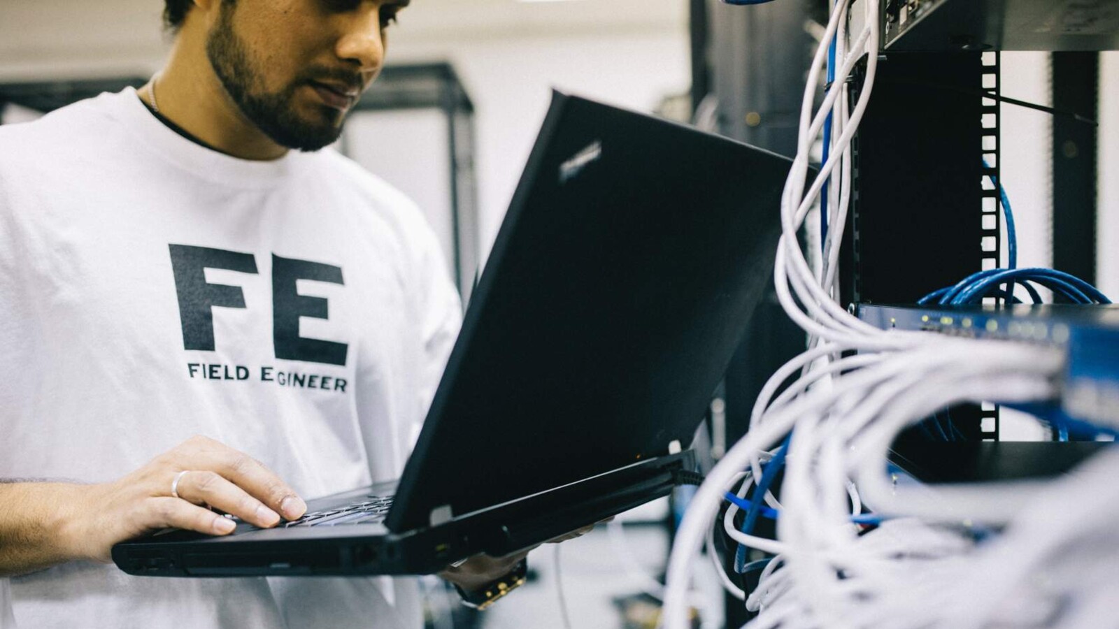 Person holding laptop, standing beside cable racks.