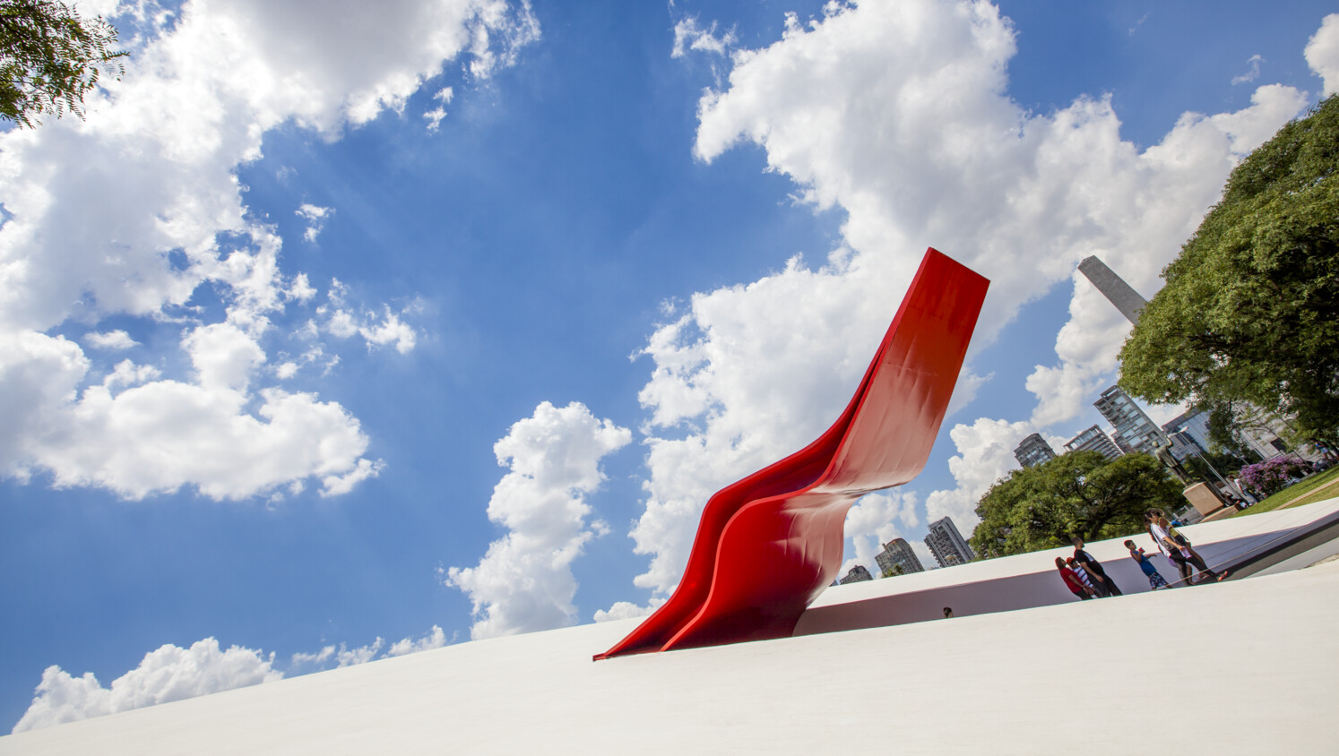 Red abstract sculpture with people, trees, and skyline.