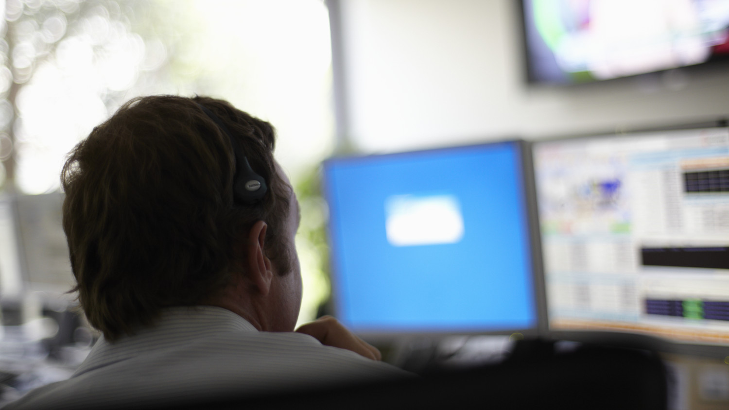 Back of a mans head while he looks at a blue computer screen in the background.